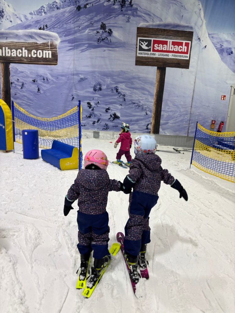 Kinder im Übungsbereich einer Skihalle, von hinten fotografiert