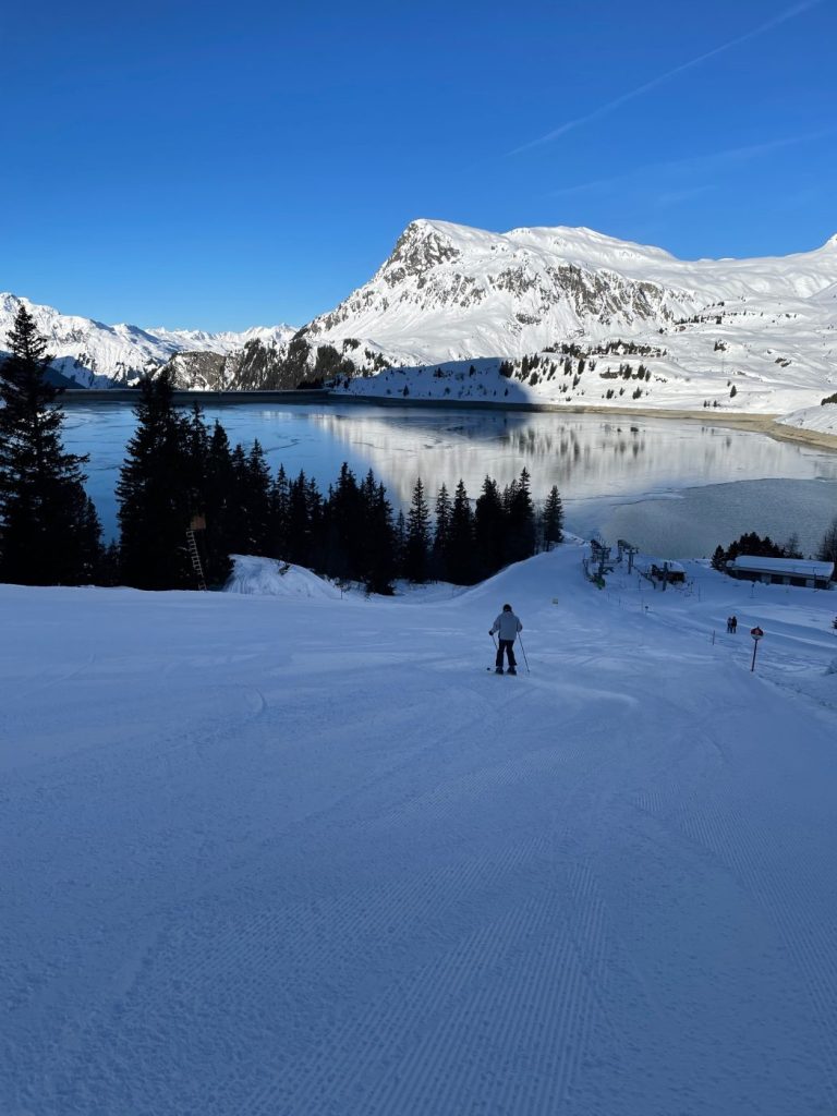 Verschneiter Bergsee mit Gipfeln und Nadelwald im Skigebiet